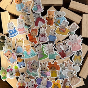 May include: A selection of colourful stickers featuring animal characters in detailed outfits. The stickers include bears, bunnies, cats, and other animals dressed in costumes and clothing. The stickers are scattered on a wooden surface.