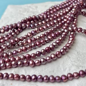 May include: A strand of purple freshwater pearls. The pearls are round and have a slight iridescent sheen.
