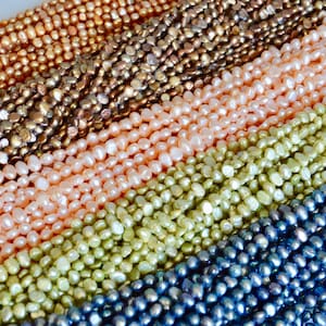 May include: A close-up of five strands of freshwater pearls. The pearls are all different colors, including white, pink, green, and blue. The pearls are all irregular in shape and have a slightly matte finish.