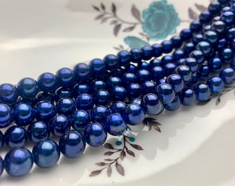 Puede incluir: Una hebra de cuentas de vidrio azul oscuro con un acabado de alto brillo. Las cuentas son redondas y de tamaño uniforme.