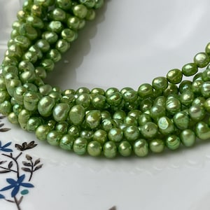 May include: A strand of green freshwater pearls. The pearls are round and have a slight iridescent sheen.