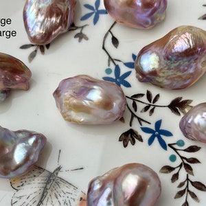 May include: A collection of large, irregularly shaped pearls with iridescent surfaces. The pearls display a range of colors, including pink, purple, and gold, and are arranged on a white plate with blue floral designs. The text "Large X-Large" is visible.