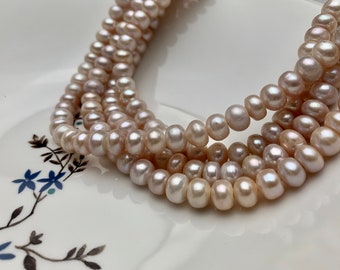 May include: A strand of pale pink freshwater pearls, with a slightly irregular shape, arranged in a loose pile on a white plate with a floral design.
