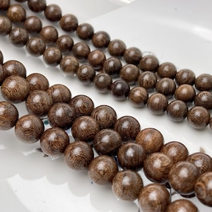 May include: A strand of dark brown wooden beads, each bead is round and has a smooth, polished finish. The beads are strung together on a cord and are arranged in a loose, flowing pattern.