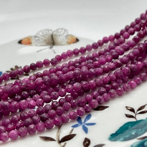 May include: A strand of deep pink faceted gemstone beads. The beads are small and round, and they are strung together on a clear thread.