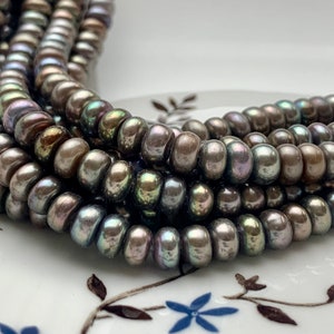 May include: A strand of iridescent black freshwater pearls. The pearls are round and have a smooth, glossy finish. They are strung on a clear thread.