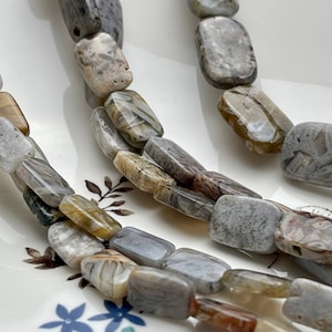 May include: A strand of light gray, brown, and white agate beads. The beads are rectangular and have a natural, polished finish.