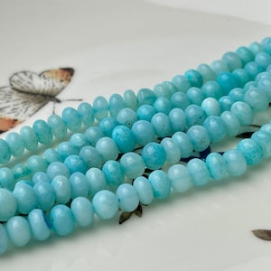 May include: A strand of light blue aquamarine beads. The beads are round and have a smooth, polished finish.