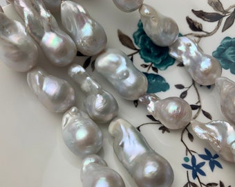 May include: A strand of white baroque pearls with iridescent highlights. The pearls are irregular in shape and have a smooth, glossy finish.