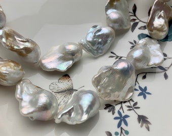 May include: A strand of white and cream baroque pearls with iridescent sheen. The pearls are irregular in shape and have a natural, organic look.