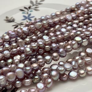 May include: A strand of lavender-colored freshwater pearls. The pearls are irregular in shape and have a slightly iridescent sheen.