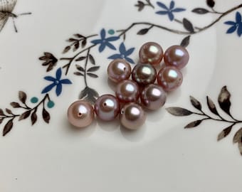 May include: A collection of iridescent pink pearls, some with a slight green hue, arranged on a white surface with a floral pattern.