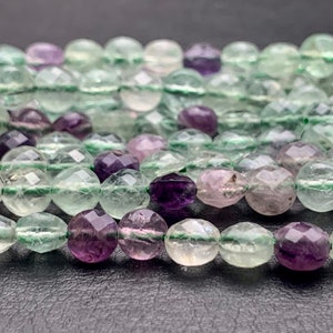May include: A strand of faceted fluorite beads in shades of green, purple, and pink. The beads are round and have a smooth, polished finish.