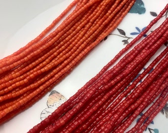 Puede incluir: Dos hebras de cuentas de coral, una hebra es de color naranja claro y la otra es de color rojo oscuro. Las cuentas son pequeñas y redondas.