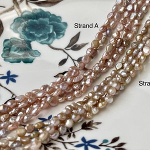 May include: Two strands of freshwater pearls, one strand labeled "Strand A" and the other labeled "Strand B". The pearls are a mix of pink, white, and cream colors and have an irregular shape.