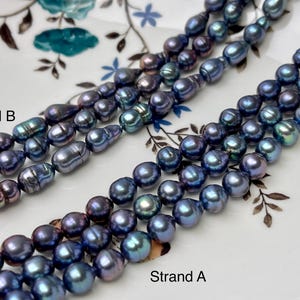 May include: Two strands of iridescent blue freshwater pearls. Strand A features round pearls, while Strand B features baroque pearls.  The pearls are displayed on a white plate with a floral pattern.