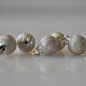 May include: Four silver-toned metal beads with a textured surface. Each bead has a small loop on the side for attaching to a necklace or bracelet.