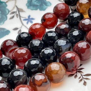 May include: A strand of faceted agate beads in shades of red, black, and brown. The beads are round and have a polished finish.