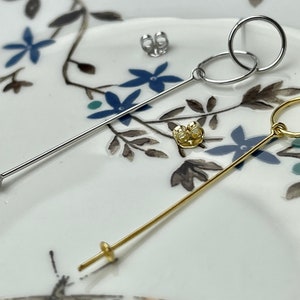 May include: Two earring posts with different styles of hoops. One post is gold and has a double hoop design. The other post is silver and has a single hoop design.