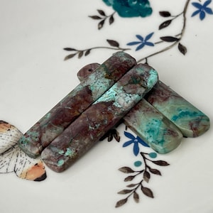 Puede incluir: Tres piedras largas, rectangulares y pulidas con una mezcla de colores marrón, verde y azul. Las piedras tienen un patrón de mármol y están apiladas unas sobre otras.