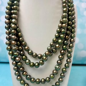May include: A multi-strand necklace featuring numerous round, dark olive-green pearls with a metallic luster. The pearls are strung in several cascading layers, creating a voluminous appearance with consistent sizing and a smooth, reflective surface finish.