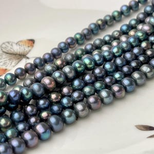 May include: A strand of dark blue iridescent pearls. The pearls are round and smooth, and they have a slight green sheen.