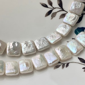 May include: A strand of white square-shaped pearl beads. The pearls have an iridescent sheen.