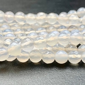 May include: A strand of white agate beads with a faceted finish. The beads are round and have a translucent appearance.