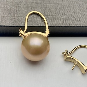 May include: A pair of gold-tone earrings with a large, round, cream-colored pearl. The earrings have a simple, elegant design.