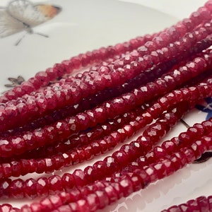May include: A strand of deep red faceted gemstone beads. The beads are small and round, and they are strung together on a clear thread.