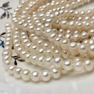 May include: A strand of white pearl beads, arranged in a circular pattern on a white surface with a floral design.