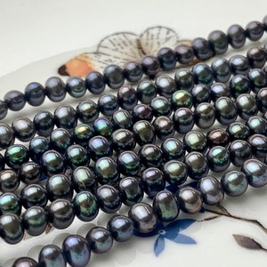 May include: A strand of black pearls with iridescent green and blue hues. The pearls are round and smooth, and they are strung on a clear thread.