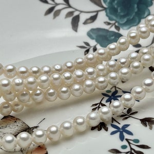 May include: Several strands of small, round, white pearls are arranged on a decorative plate. The pearls have a luminous sheen. The plate has a floral design with blue and white accents.