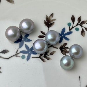 Könnte beinhalten: Sechs schimmernde graue Perlen auf weißem Hintergrund mit floralem Muster.