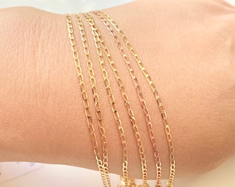 Puede incluir: Primer plano de seis cadenas de oro de diferentes anchos, superpuestas en el brazo de una persona. Las cadenas están hechas de un diseño fino, delicado e intrincado.