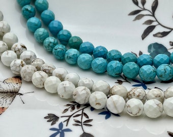 May include: Two strands of faceted beads, one white and one turquoise, are displayed on a white plate with a floral pattern. The beads are round and have a slightly irregular shape.