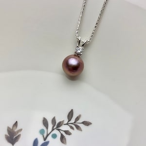 May include: A silver chain necklace with a single, large, iridescent purple pearl pendant and a small, clear, round gemstone accent.