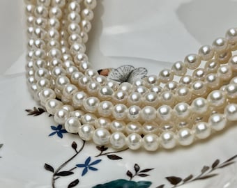 May include: A strand of white freshwater pearls, with a smooth, round shape. The pearls are arranged in a loose, flowing pattern, creating a delicate and elegant look.