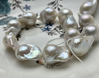 May include: A strand of white baroque pearls with iridescent highlights. The pearls are strung on a white thread and are arranged in a circular pattern.