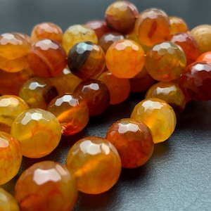 May include: A strand of carnelian beads, each bead is faceted and has a unique orange and brown color pattern.