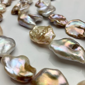 Puede incluir: Una hebra de perlas barrocas en varios tonos de blanco, crema y dorado. Las perlas son de forma irregular y tienen un brillo lustroso.