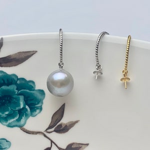 May include: Two silver and one gold earring findings with a single white pearl on one of the silver findings.