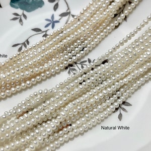 May include: Two strands of white freshwater pearls, one strand labeled "Cream White" and the other labeled "Natural White". The pearls are small and round, and they are arranged in a straight line on a white surface.