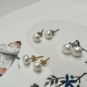 Puede incluir: Tres pares de pendientes de perlas en un plato decorativo. Dos pares tienen postes de plata y un par tiene postes de oro. Las perlas son blancas y redondas. El plato tiene un diseño de mariposa y floral.