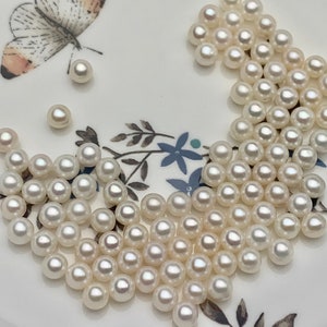 May include: A collection of white round pearls on a white plate with a floral design. The pearls are various sizes and are scattered across the plate.
