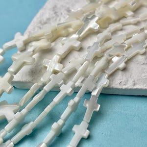 May include: A strand of white mother of pearl cross beads. The beads are strung on a white cord and are all the same size and shape.