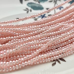 May include: Close-up of multiple strands of delicate, light pink seed beads. The beads are small and evenly spaced, creating a textured, layered effect. The beads are likely used for jewelry making or other crafts.