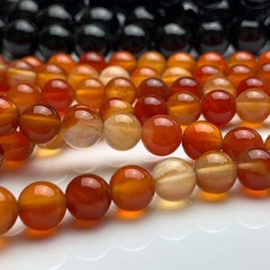 May include: A strand of carnelian beads in shades of orange and red. The beads are round and smooth, and they are strung on a clear thread.