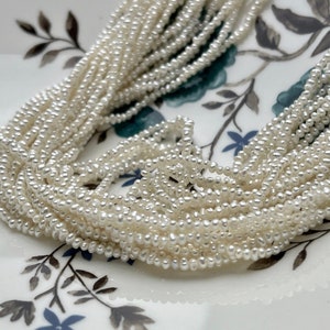 May include: A strand of white freshwater pearls, arranged in a pile on a white plate with a floral pattern.