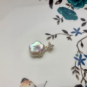 May include: A white flower-shaped pearl pendant with a gold setting and clear crystal accents.